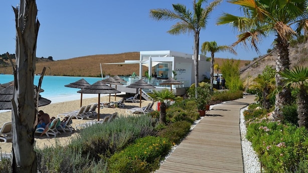 Un complexe hôtelier en bord de mer doté d’une piscine, de chaises longues, de palmiers et d’une promenade en bois.