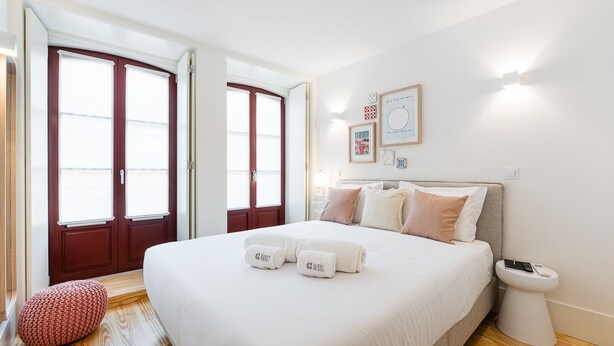 A modern hotel room with a large bed, two doors, a bedside table, and a small stool. - GuestReady - Clérigos Tiles House (Porto)