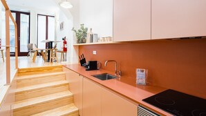 A modern kitchen with a wooden staircase, a sink, and a black induction cooktop. - GuestReady - Clérigos Tiles House (Porto)