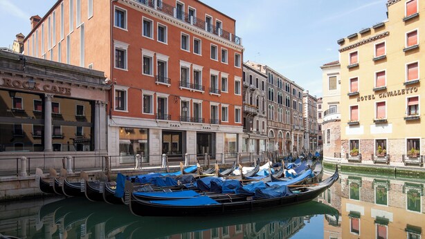A canal with gondolas docked along the side of a building with Zara and Hotel Cavallotto signs.