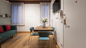 A dining area with a wooden table, blue chairs, a vase with flowers, and a green sofa with red cushions.