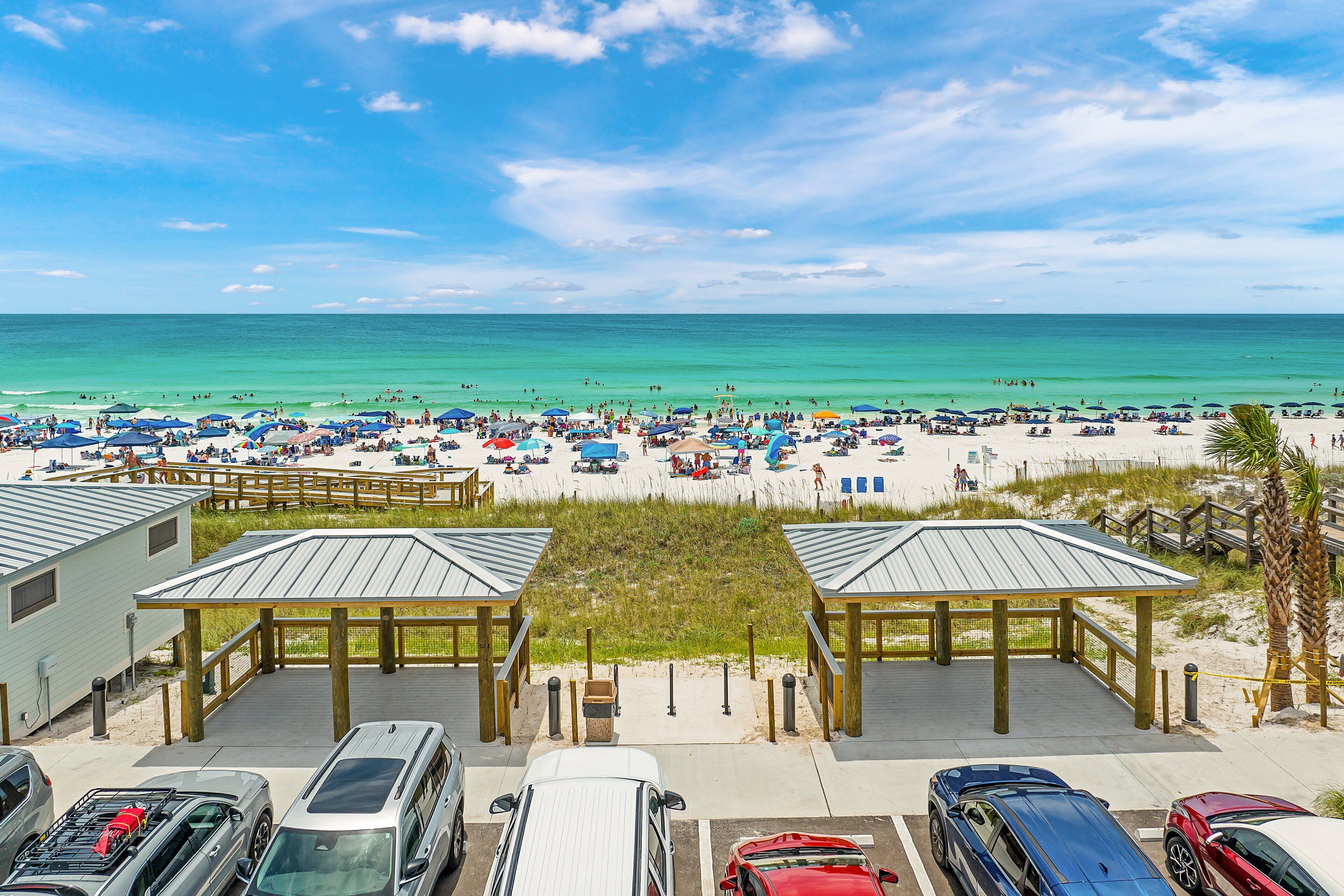 Une plage avec vue sur la mer, un espace de stationnement, des parasols et des personnes se prélassant sur la plage.