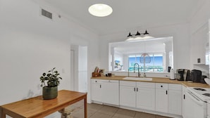 A modern kitchen with white cabinets, a wooden table, and a view of the city through the window. - Le Petit Italie Water View 2 2 With Pool (Sunny Isles Beach)