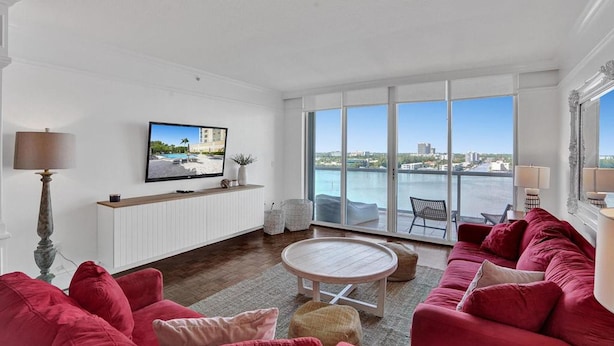 A spacious living room with a large window overlooking a body of water and cityscape. - Le Petit Italie Water View 2 2 With Pool (Sunny Isles Beach)