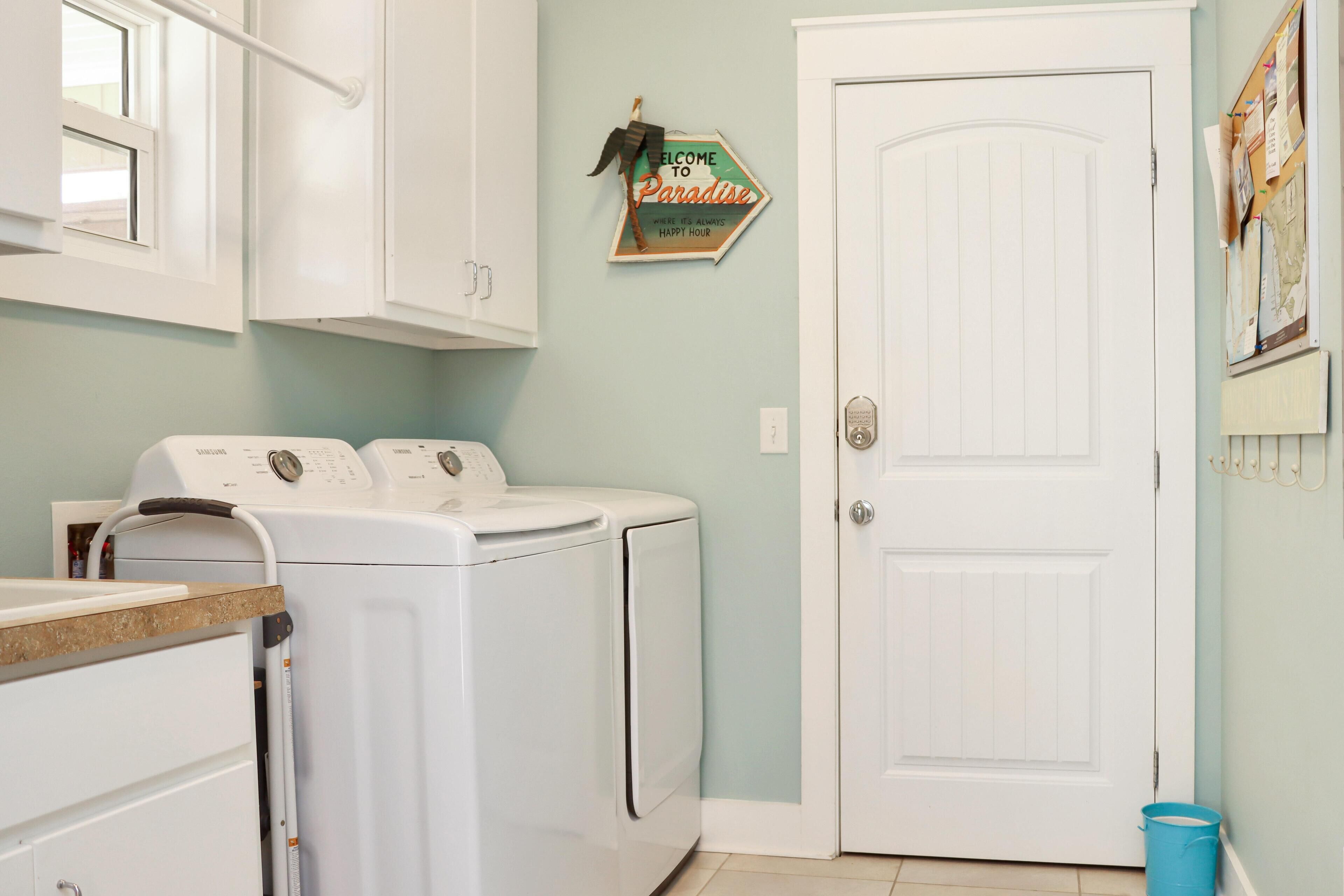 A laundry area with two white washing machines, a door, and a welcome sign.