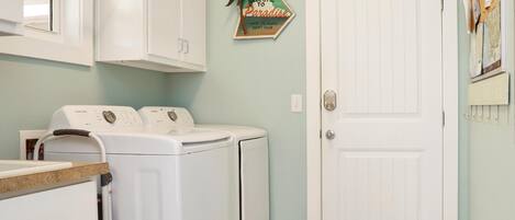 A laundry area with two white washing machines, a door, and a welcome sign.