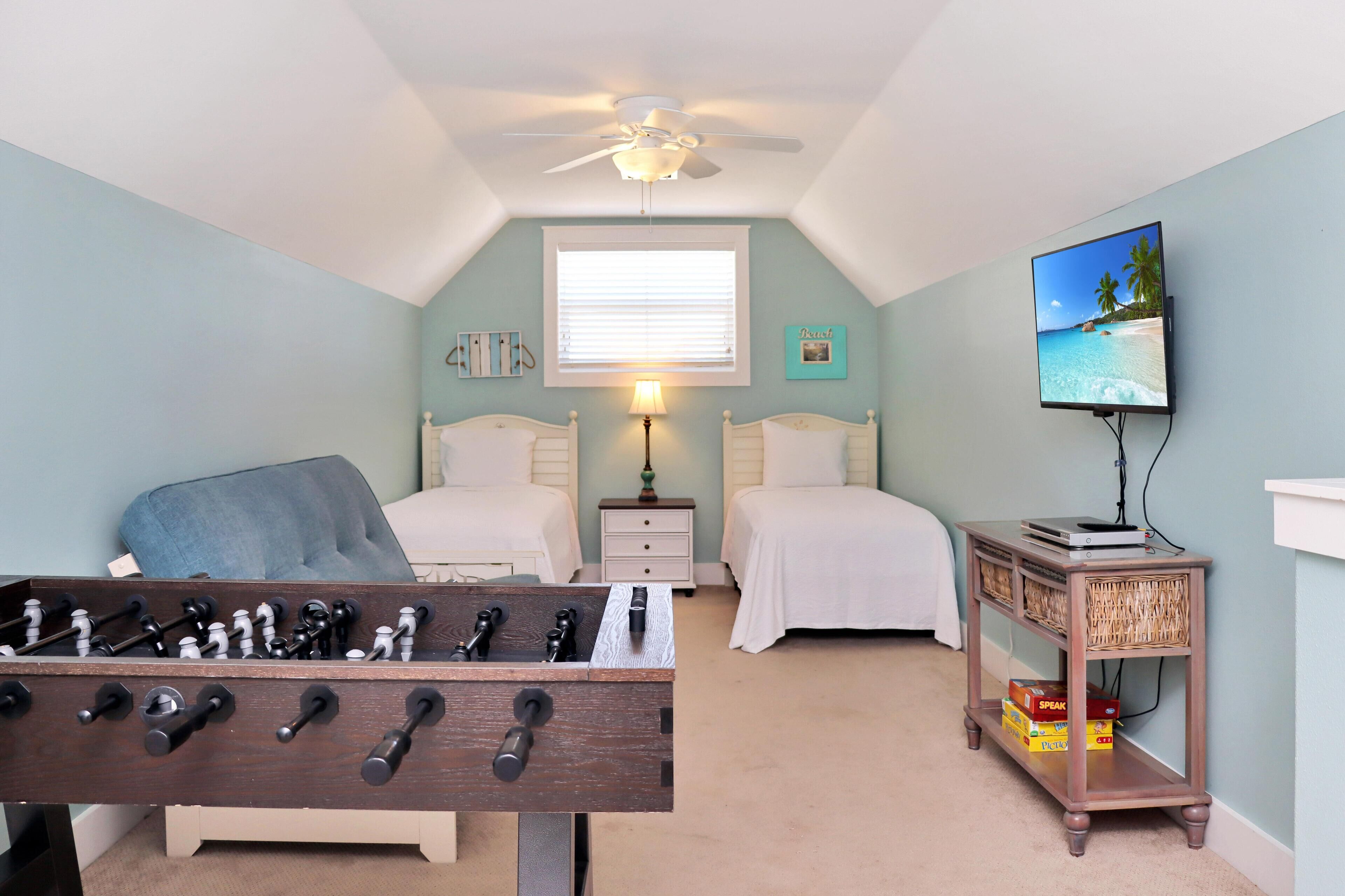 A bedroom with two beds, a ceiling fan, a TV, and a small table with a board game.