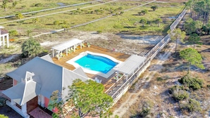A house with a swimming pool, surrounded by a wooden deck and a beach view.