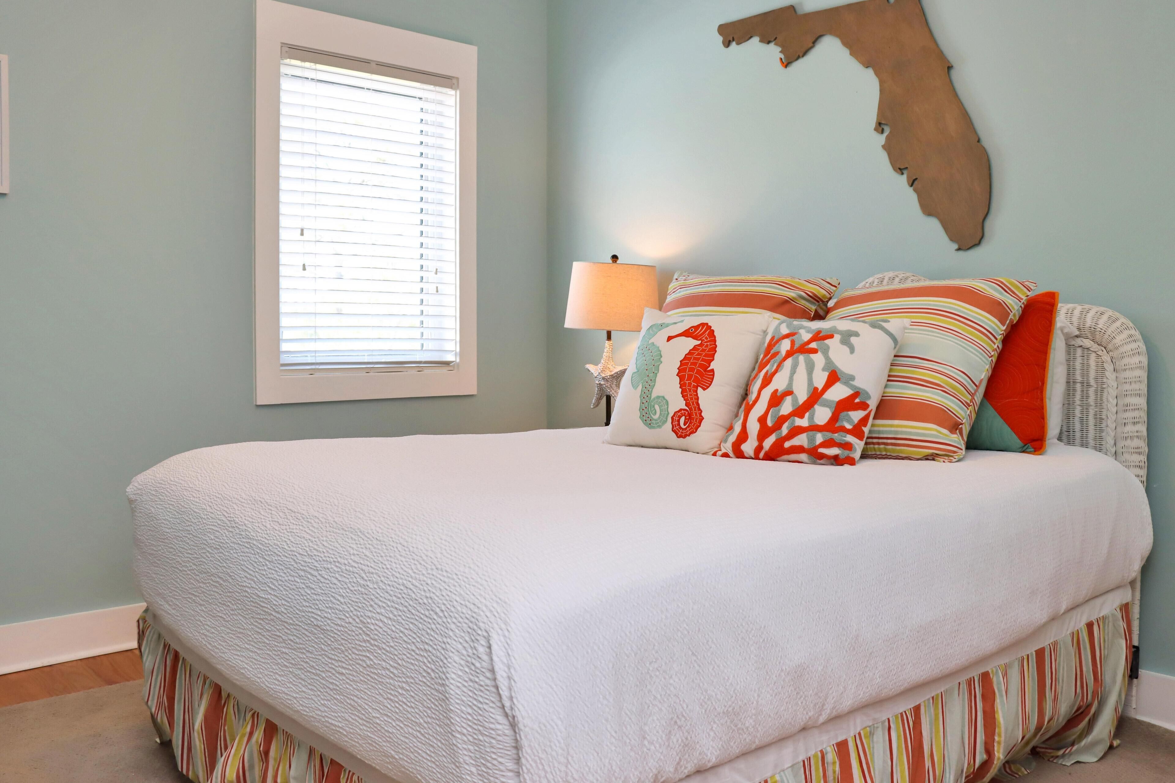 A bedroom with a large bed, striped bedding, a seahorse pillow, a lamp, and a wall map.