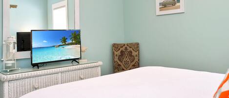 A bedroom with a bed, a television on a glass-top dresser, a mirror, and a framed picture on the wall.