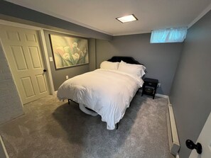 Una camera da letto con un letto, un comodino, un quadro, una porta e una finestra con tenda.