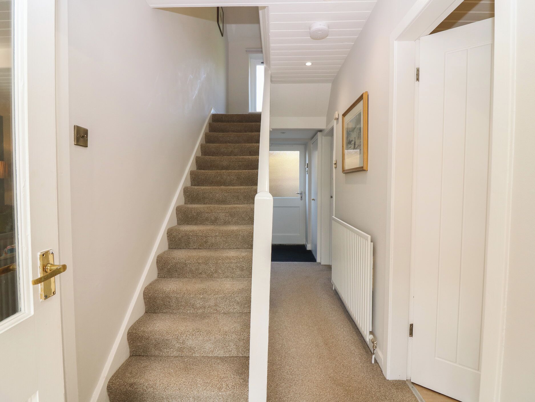 A hallway with a carpeted staircase, white walls, and a radiator.