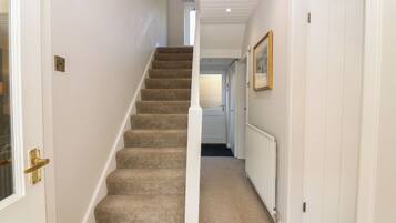 A hallway with a carpeted staircase, white walls, and a radiator.