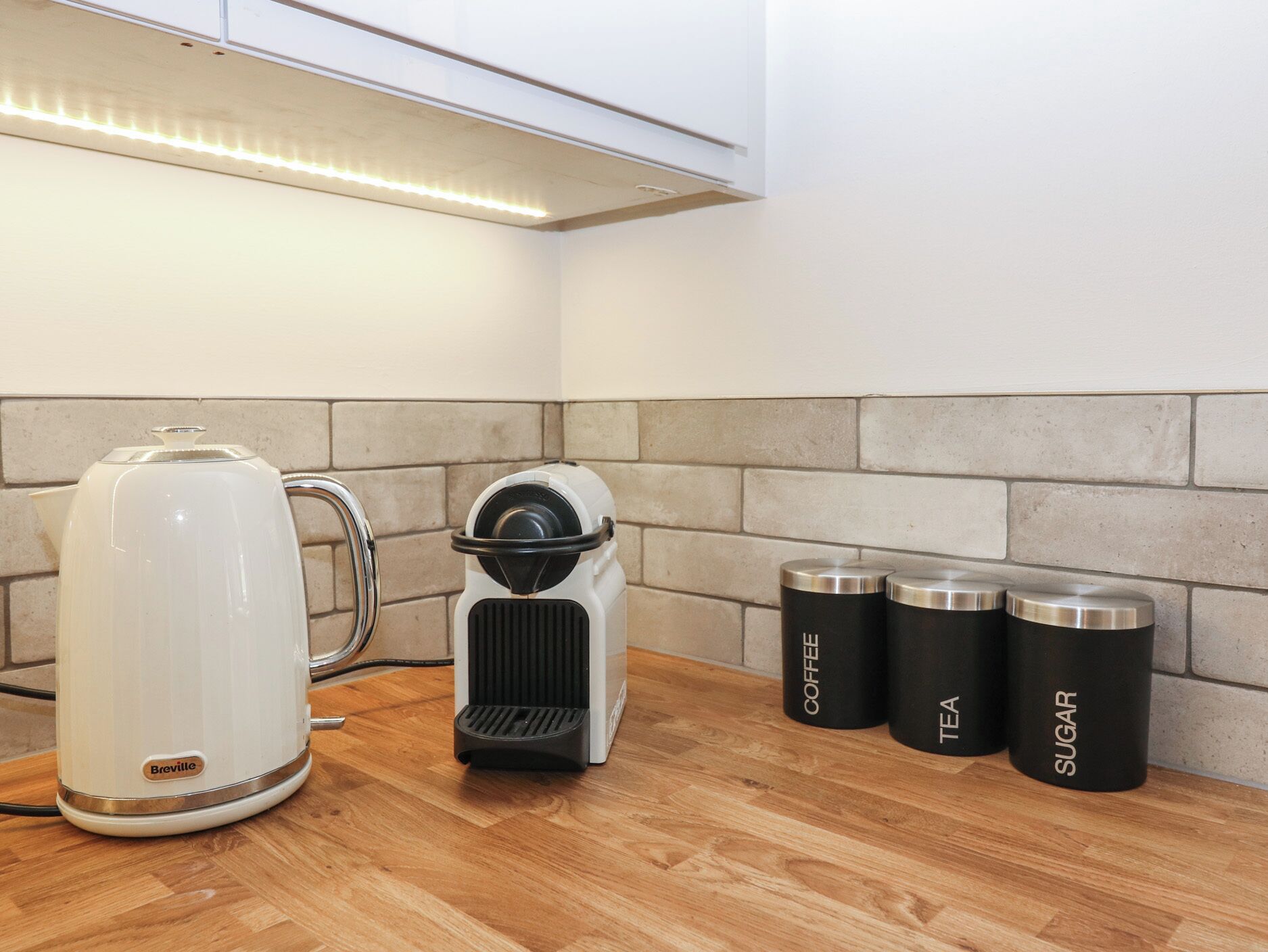 A kitchen with a Breville coffee maker, a kettle, and three containers labeled coffee, tea, and sugar.