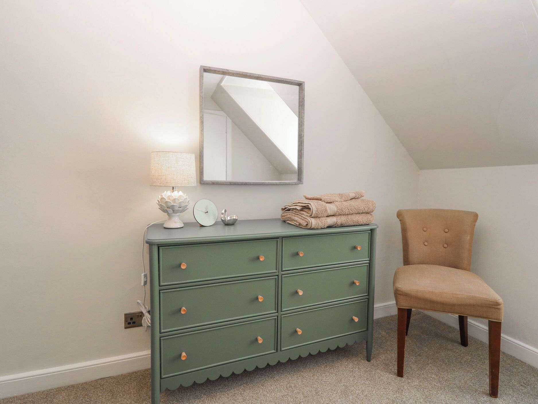 A green dresser with drawers and a mirror above it, a chair, and a lamp on the dresser.