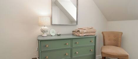 A green dresser with drawers and a mirror above it, a chair, and a lamp on the dresser.