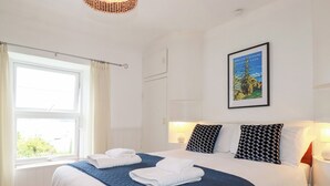 A hotel room with a large bed, two pillows, a window with curtains, a wall-mounted picture, and a bedside lamp. - Nanvivian (Truro)