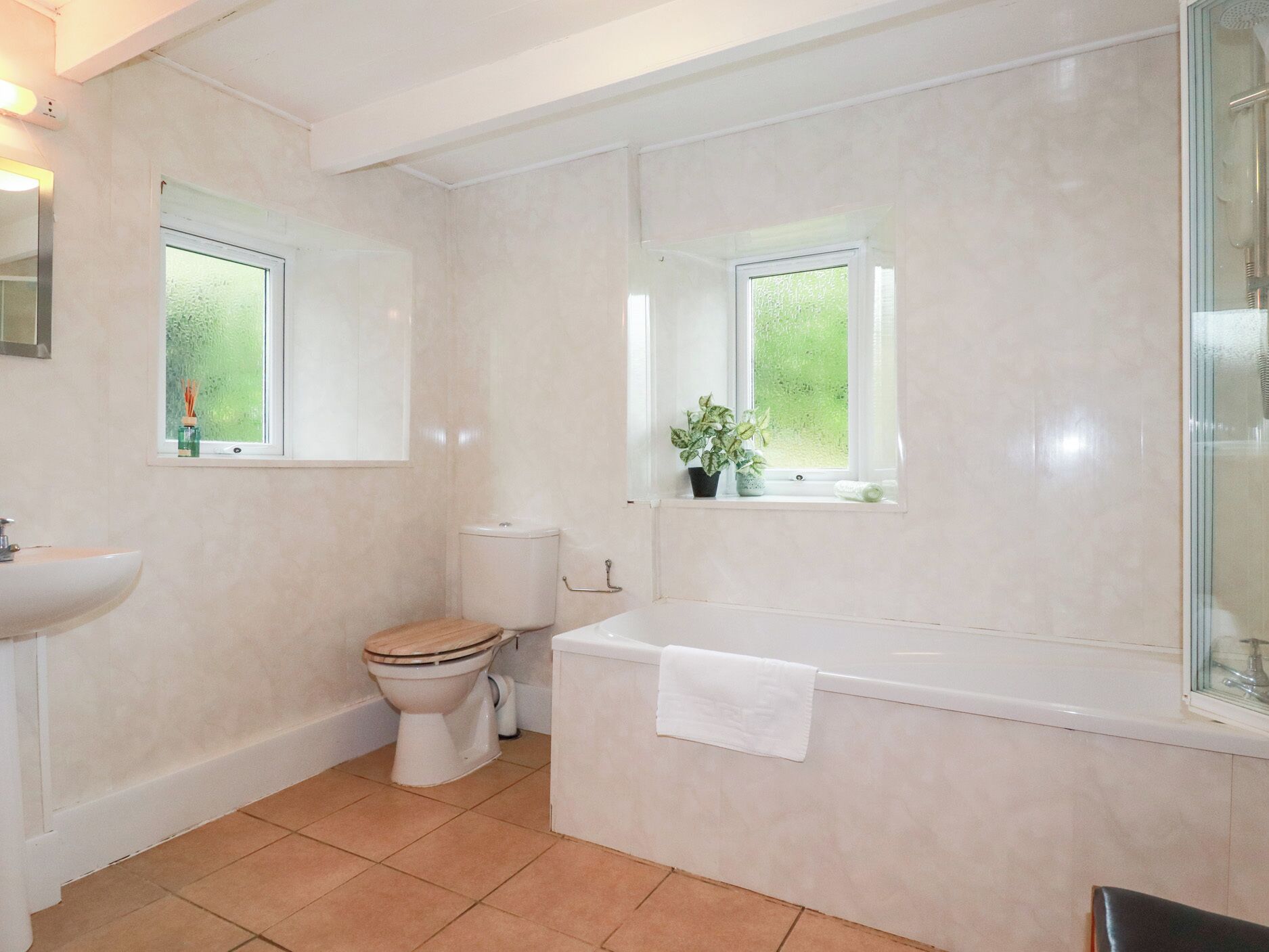 A bathroom with a toilet, sink, and bathtub. There are windows above the toilet and bathtub.