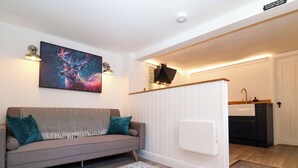A modern living room with a grey sofa, teal cushions, a patterned throw, a large abstract painting, and a white radiator.
