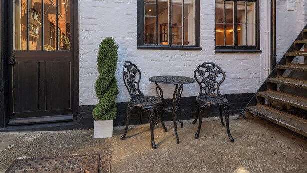A building with a white facade, a black door labeled "The Hideaway," and two windows with black frames. There is a small round table with chairs in front of the windows.