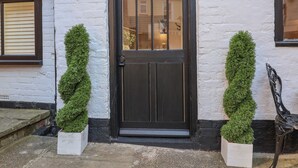 A black door with a sign above it reading "The Hideaway." There are two potted topiary plants on either side of the door.