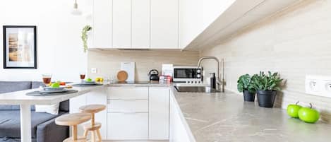 A modern kitchen with white cabinets, a marble countertop, and a dining area with a gray sofa and wooden stools.