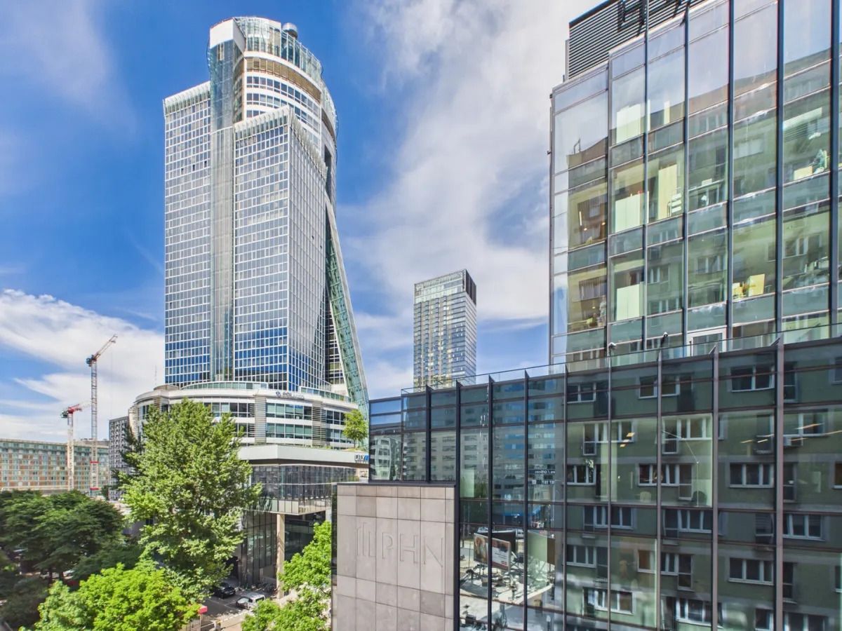 Een modern hoog gebouw met een gebogen gevel, omringd door andere hoge gebouwen en groen.