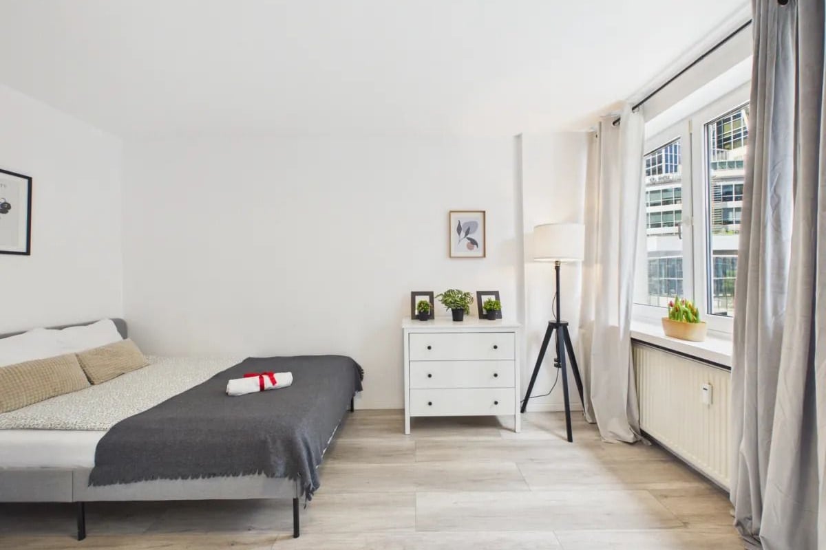 Et soveværelse med seng, sengebord, lampe og et vindue med gardiner.