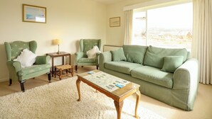 Un salon avec un canapé vert, deux fauteuils, une table basse en bois et un tapis à poils longs blanc.