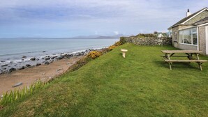 Une propriété située en bord de mer, dotée d’un mur en pierre, d’une pelouse verdoyante et d’une table de pique-nique en bois.