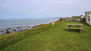 Un espace verdoyant avec un muret en pierre et un banc en bois, le tout situé au bord de la mer.