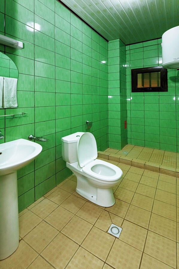 Un baño con paredes de azulejos verdes, un lavabo blanco y un inodoro.