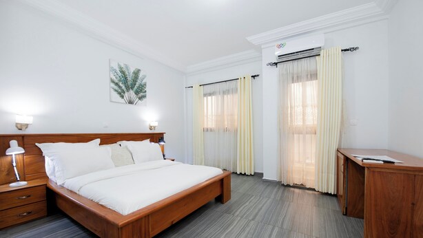 Ein Hotelzimmer mit einem hölzernen Bett, Nachttischlampen, einem Schreibtisch und einem großen Fenster mit Vorhängen.