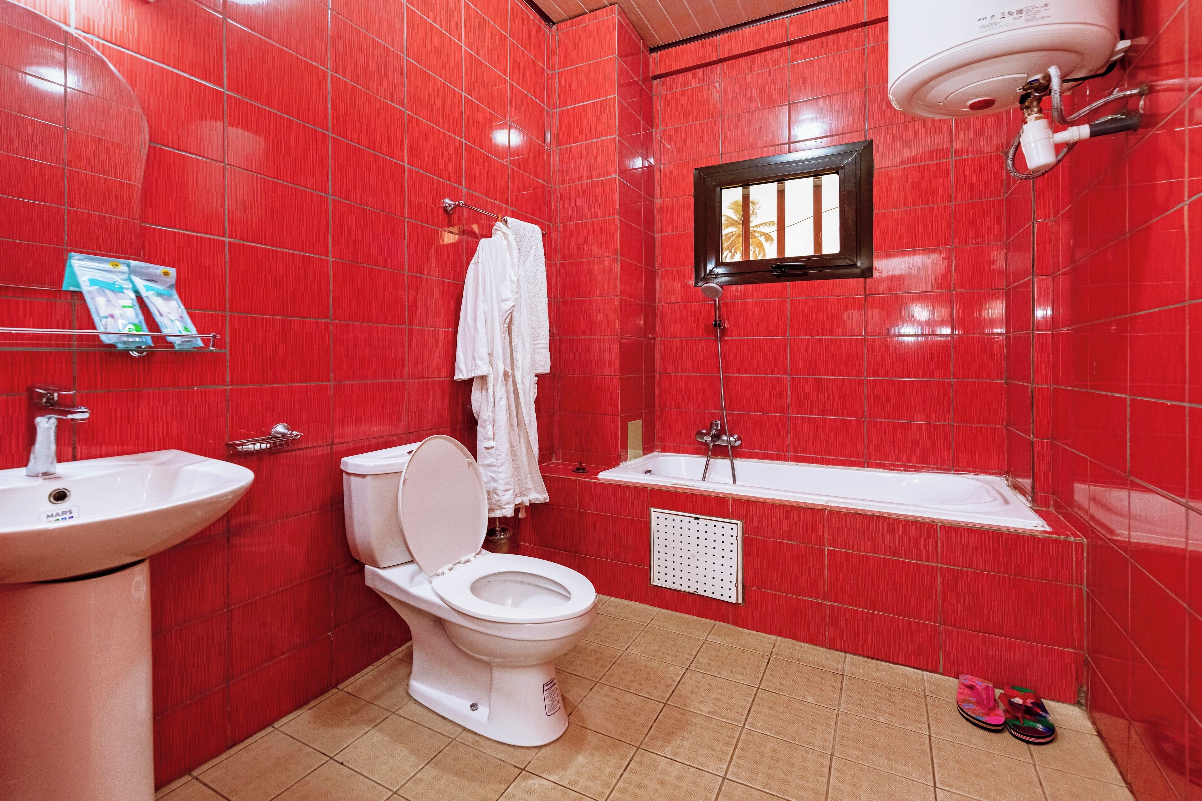 Ein Badezimmer mit roten Fliesen, einer weißen Toilette, einem Waschbecken und einer Badewanne.