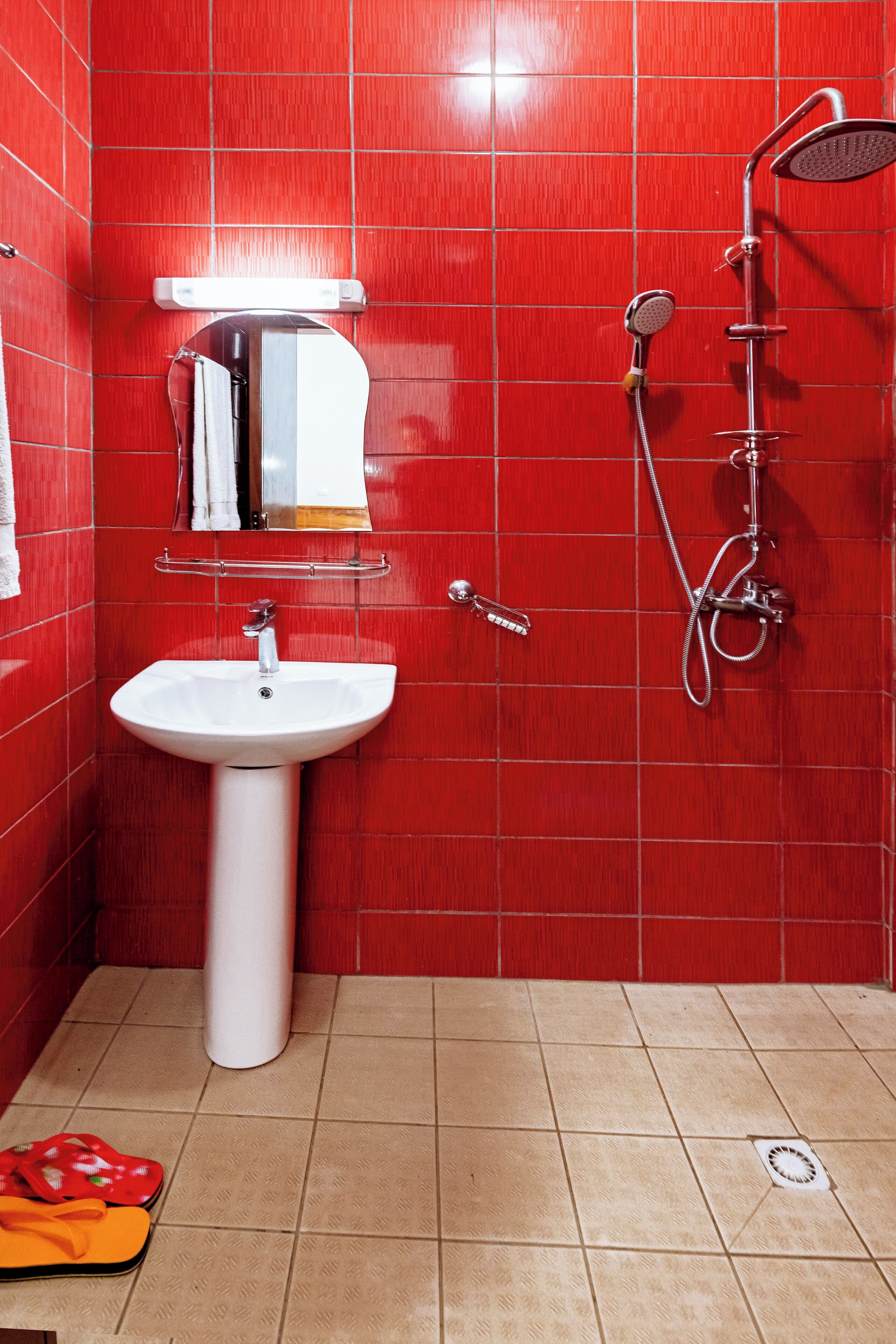Un baño con paredes de azulejos rojos, un lavamanos blanco y una ducha.