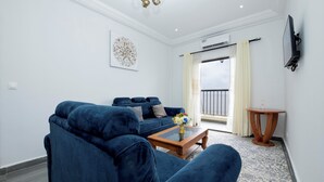 Ein modernes Wohnzimmer mit einem blauen Sofa, einem Couchtisch mit einer Vase und einem an der Wand befestigten Fernseher.