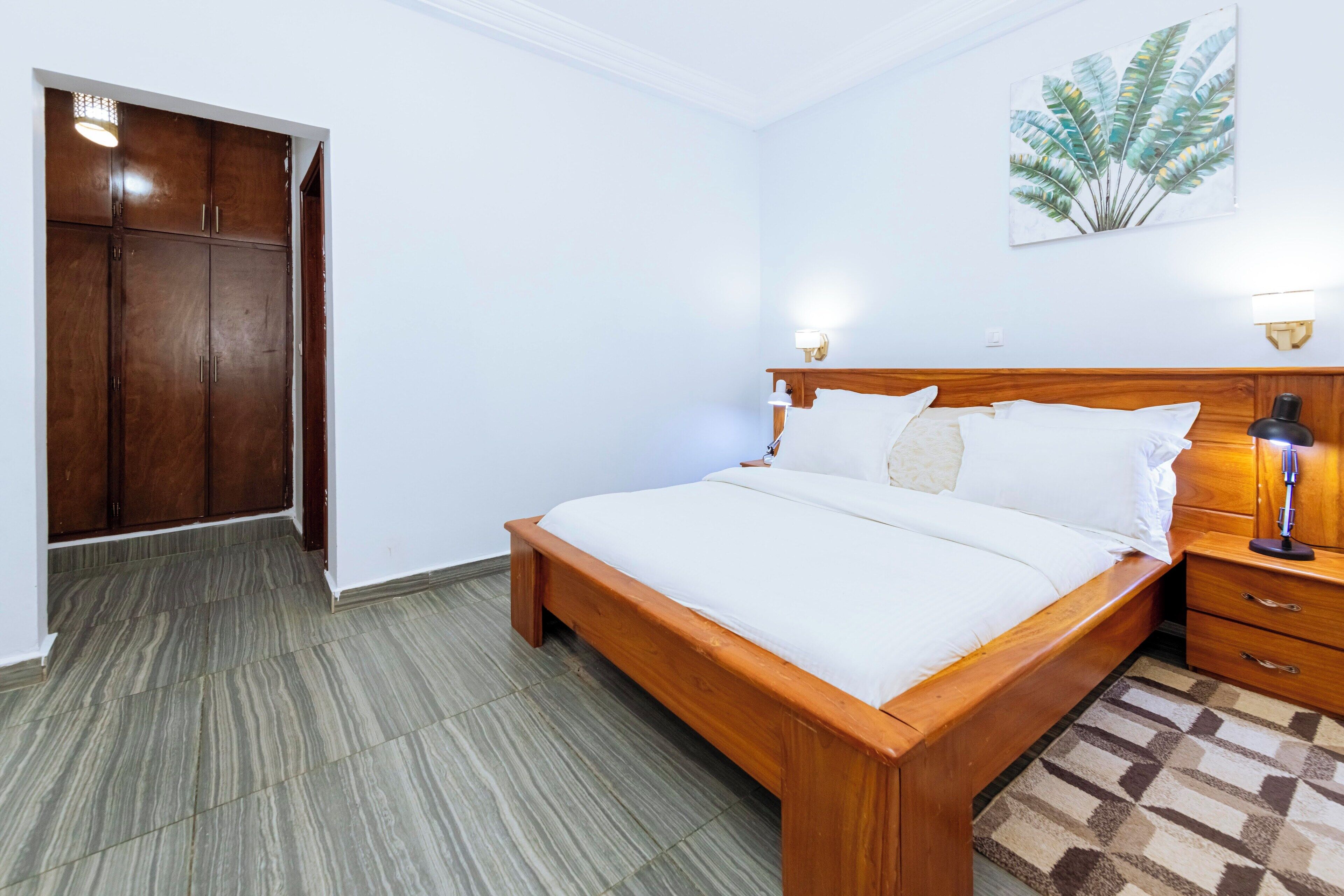 A bedroom with a wooden bed, a nightstand, a wardrobe, and a wall-mounted light fixture.