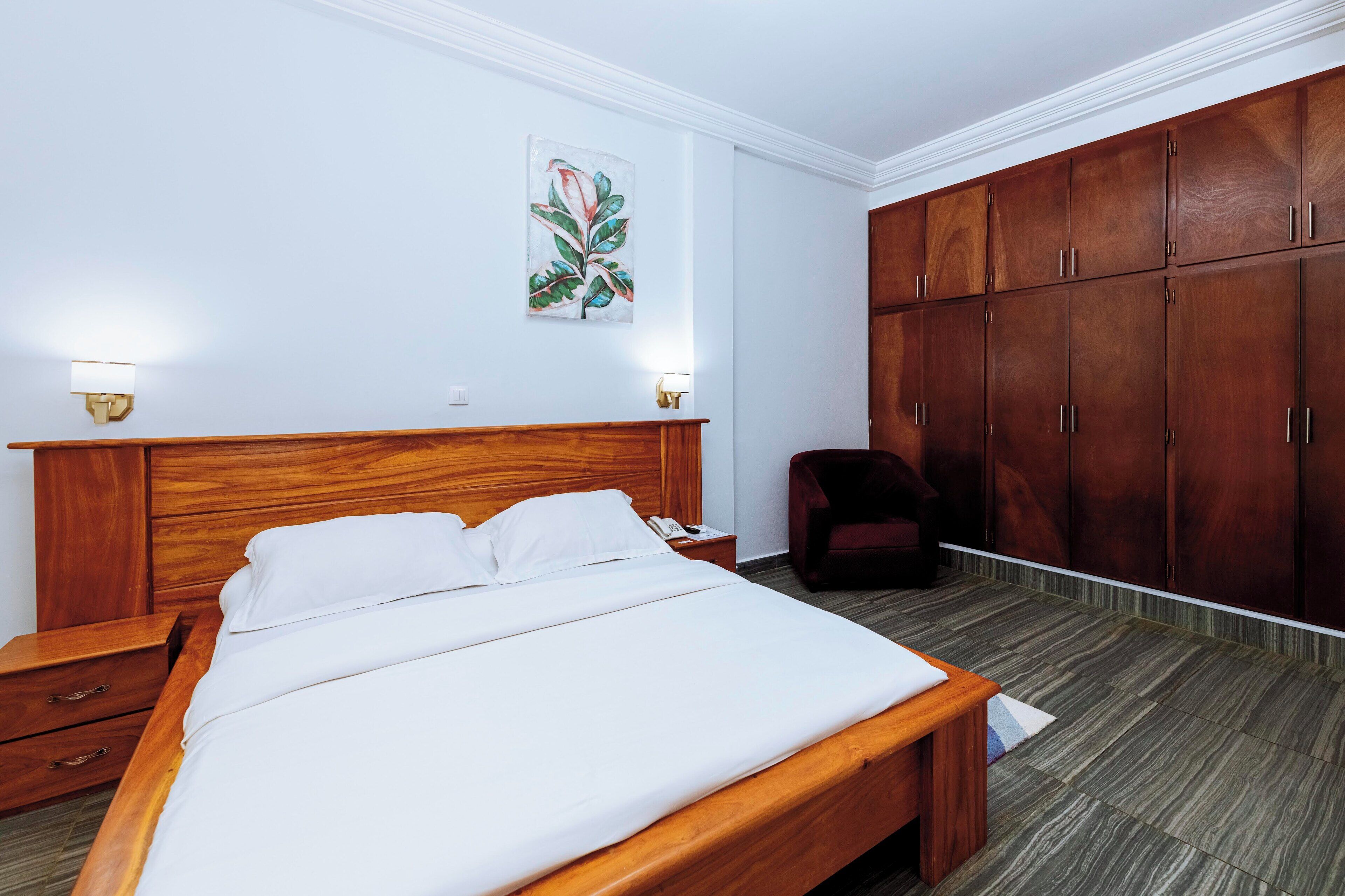 Una habitación de hotel con una cama de madera, una mesita de noche, un escritorio, una silla y un armario.