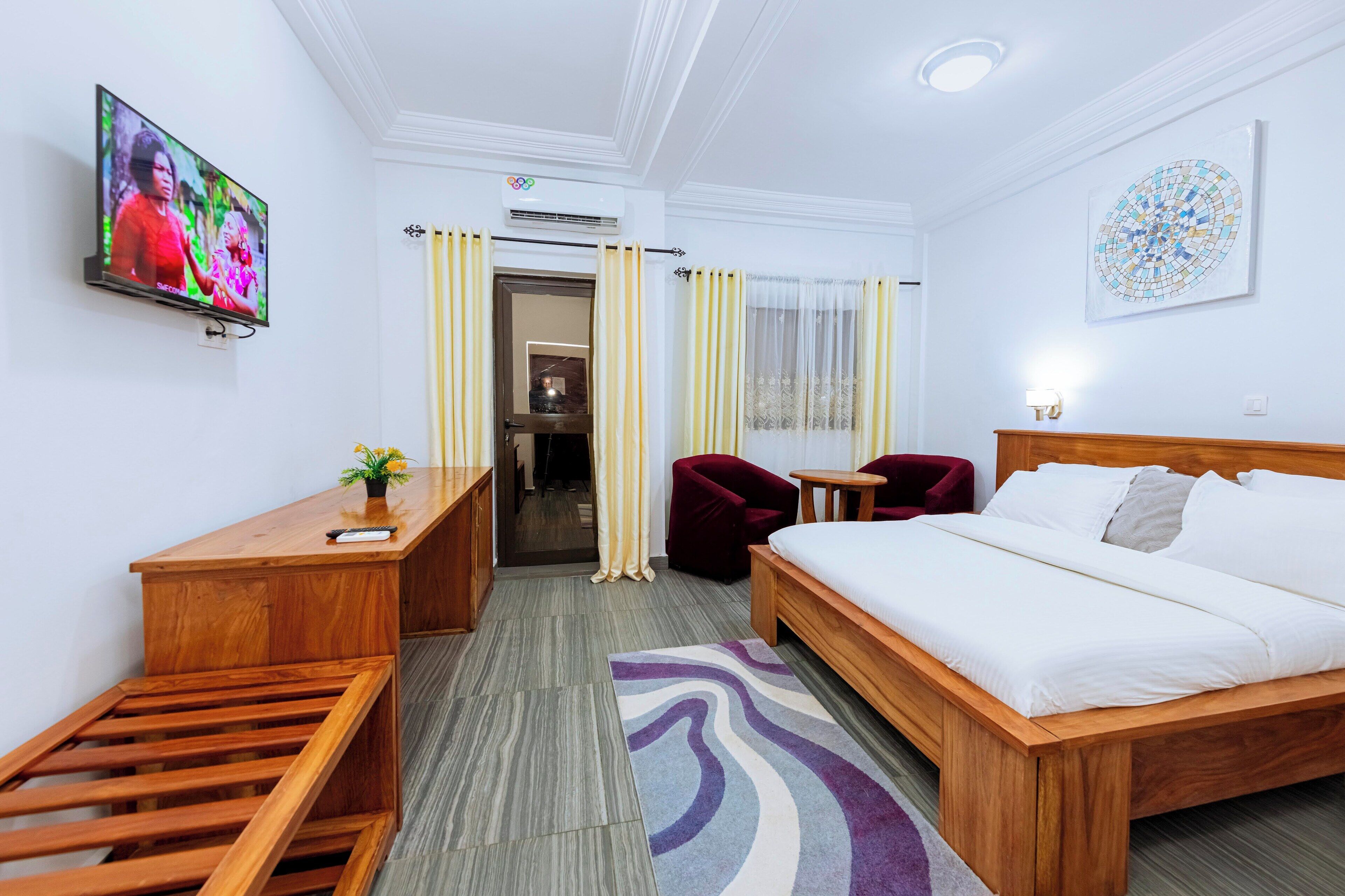 Habitación de hotel con cama, escritorio, silla, televisor y baño visible a través de una puerta.