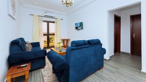 Ein Wohnzimmer mit zwei blauen Sofas, einem Couchtisch, einem Fernseher und einer Kristallleuchtre.