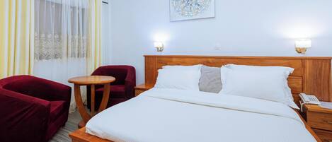 A hotel room with a wooden bed, a red armchair, a small round table, and a wall-mounted light fixture.