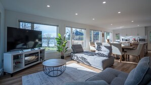 Ein modernes Wohnzimmer mit großem Fernseher, grauem Sofa und Essbereich mit Stühlen und Tisch.