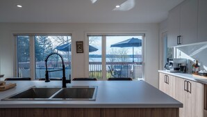 Eine moderne Küche mit einer großen Kochinsel, Holzschränken und Blick auf einen Garten durch große Fenster.