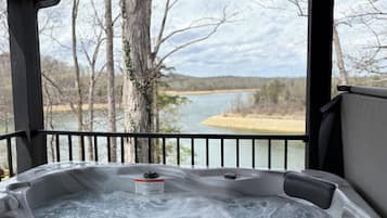 Un bain à remous agrémenté d’une étiquette d’avertissement, une terrasse en bois et une vue sur un lac et des arbres.