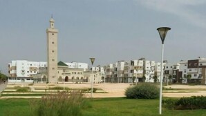 A grassy area with a tall tower and modern buildings in the background.