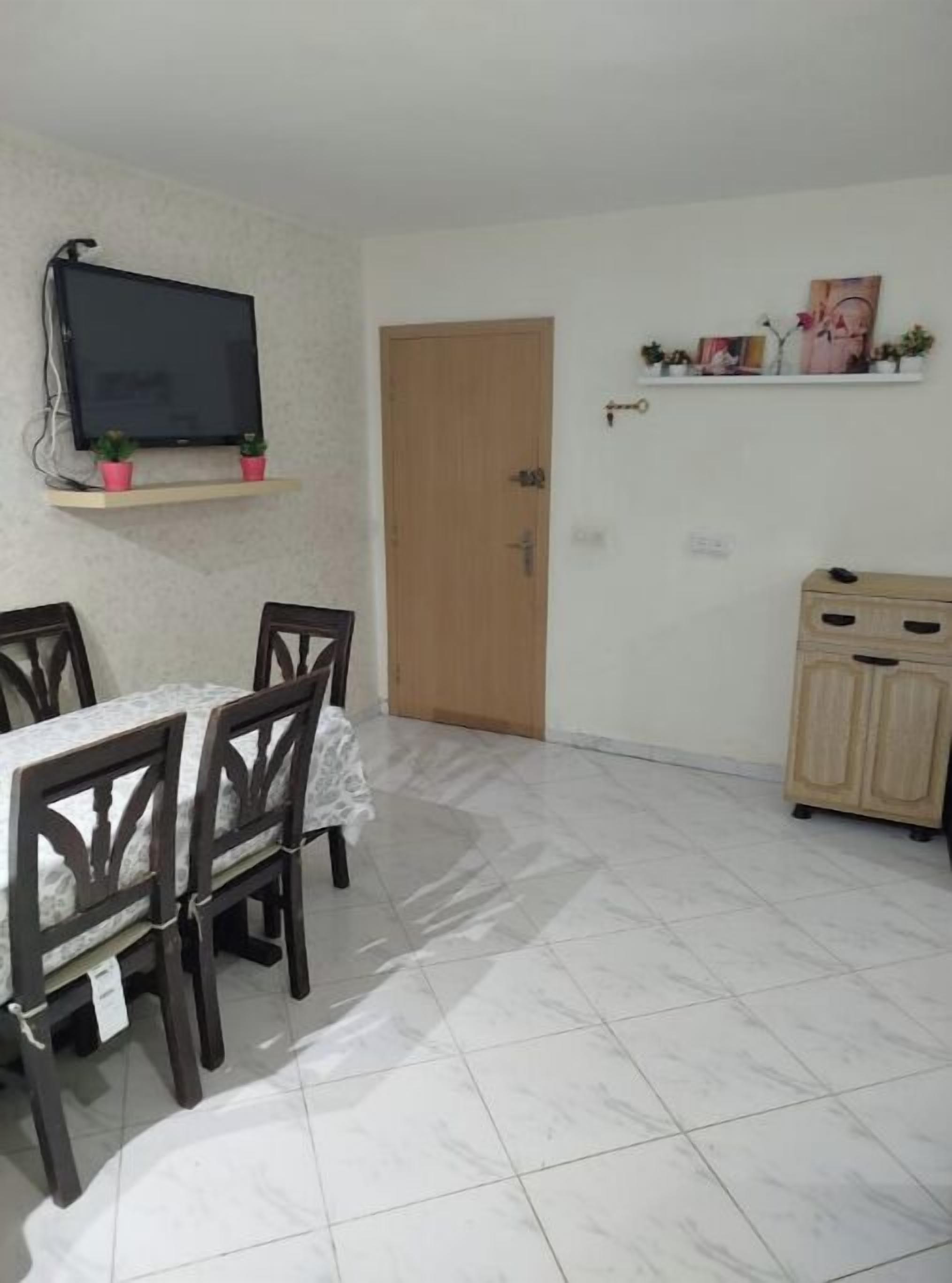 A dining area with a table and chairs, a television mounted on the wall, a wooden door, and a cabinet.