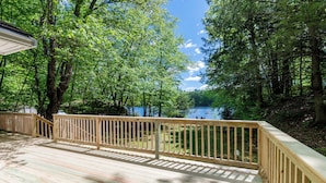 Eine Holzterrasse mit Geländer, die auf einen See mit umliegenden Bäumen blickt.