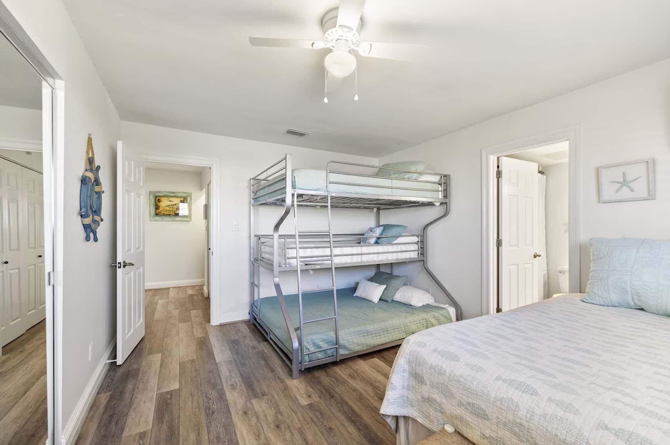 A room with bunk beds, a ceiling fan, and a door leading to another room.