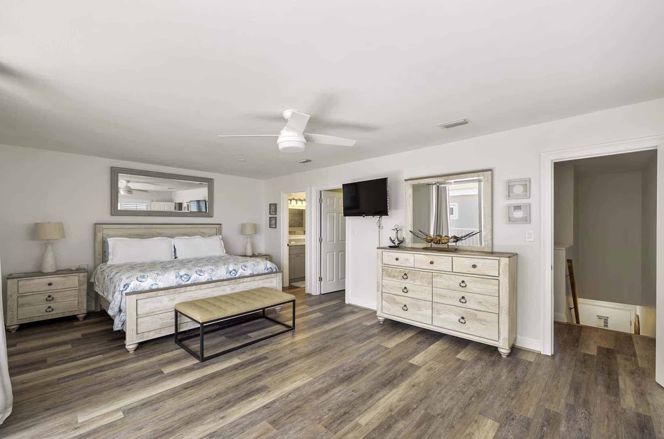 Une chambre à coucher comprenant un lit, des tables de chevet, une commode, un ventilateur de plafond et un téléviseur.