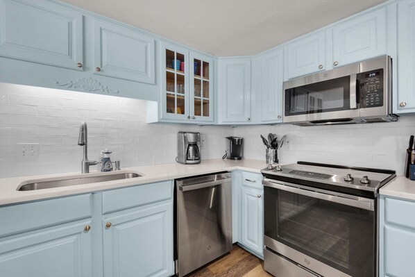 A kitchen with light blue cabinets, stainless steel appliances, and white subway tiles. - Starboard Village 121 (Pensacola Beach)